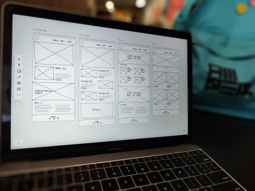 Wireframes auf einem Laptop-Bildschirm, im Hintergrund ein blauer Rucksack.