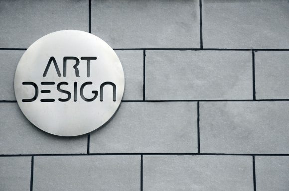 Schild mit der Aufschrift "ART DESIGN" auf einer grauen Steinwand.
