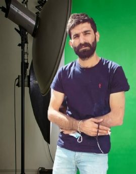 Mann mit Bart in dunkelblauem T-Shirt, vor grünem Hintergrund stehend.