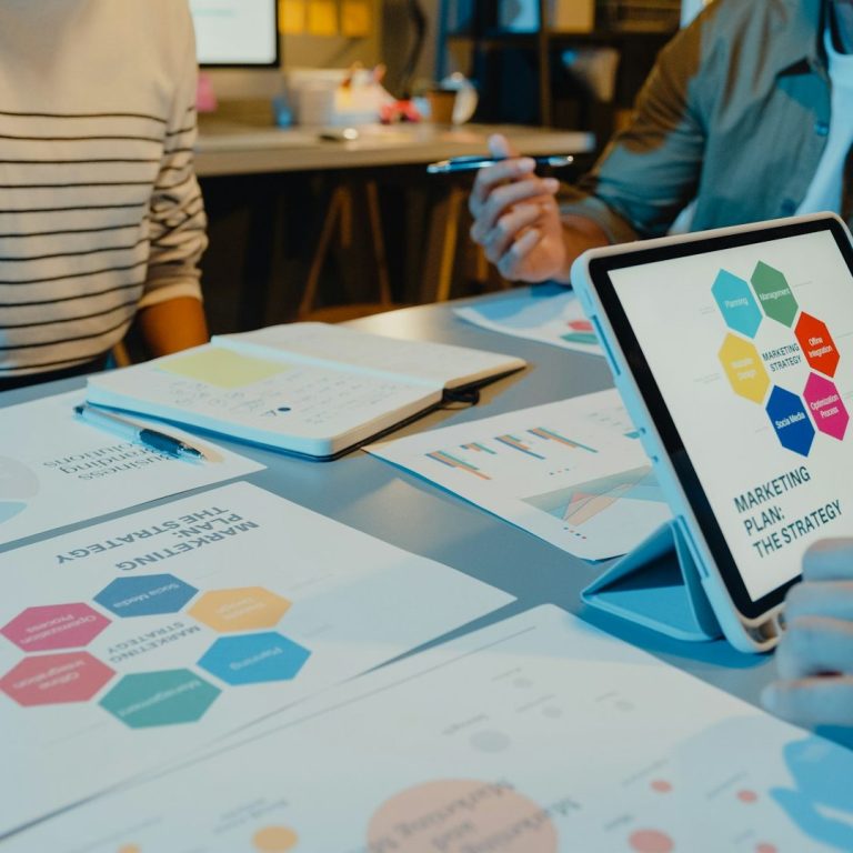 Personen analysieren Diagramme und Grafiken an einem Tisch, dabei ein Tablet im Vordergrund.
