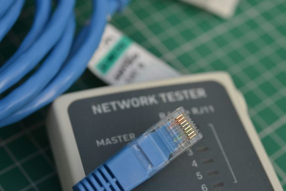 Netzwerktester mit blauer RJ45-Kabelverbindung auf einer grünen Unterlage.