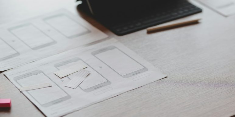 Papierlayout mit skizzierten Smartphone-Displays und Stiften auf einem Tisch.