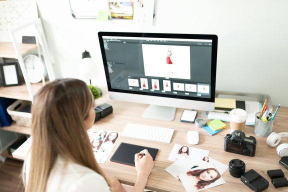 Frau arbeitet am Computer, um Designs mit Fotos und Grafiksoftware zu erstellen.