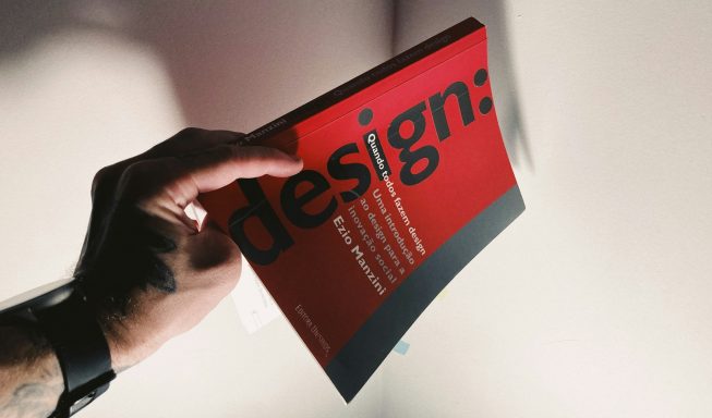 Hand hält ein rotes Designbuch mit schwarzem Schriftzug.