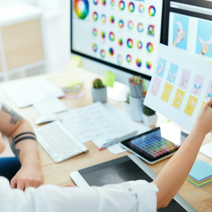 Zwei Personen arbeiten an Computerbildschirmen mit Grafiken und Farbmuster.